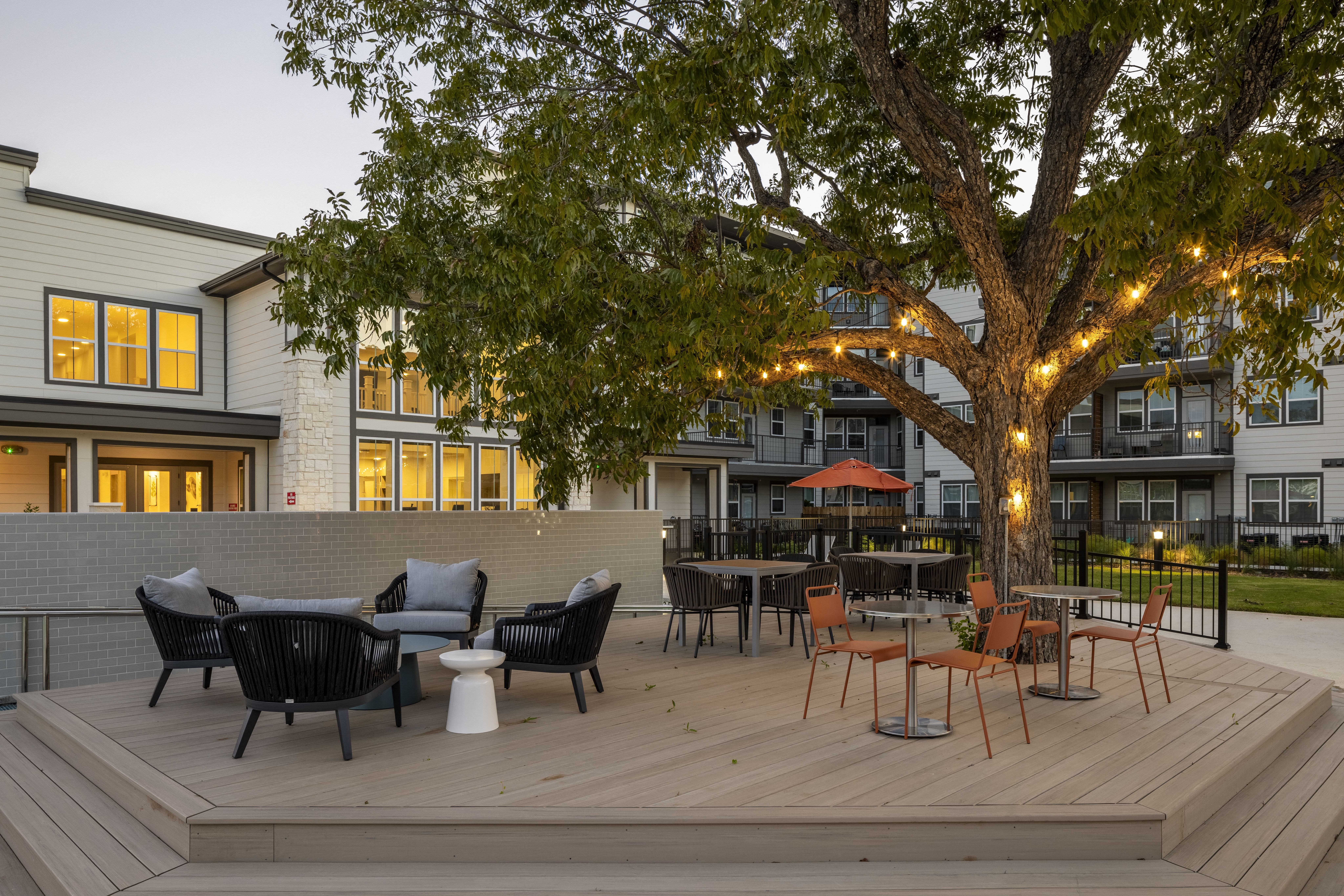 an outdoor deck with seating under a lighted tree at a senior apartment community